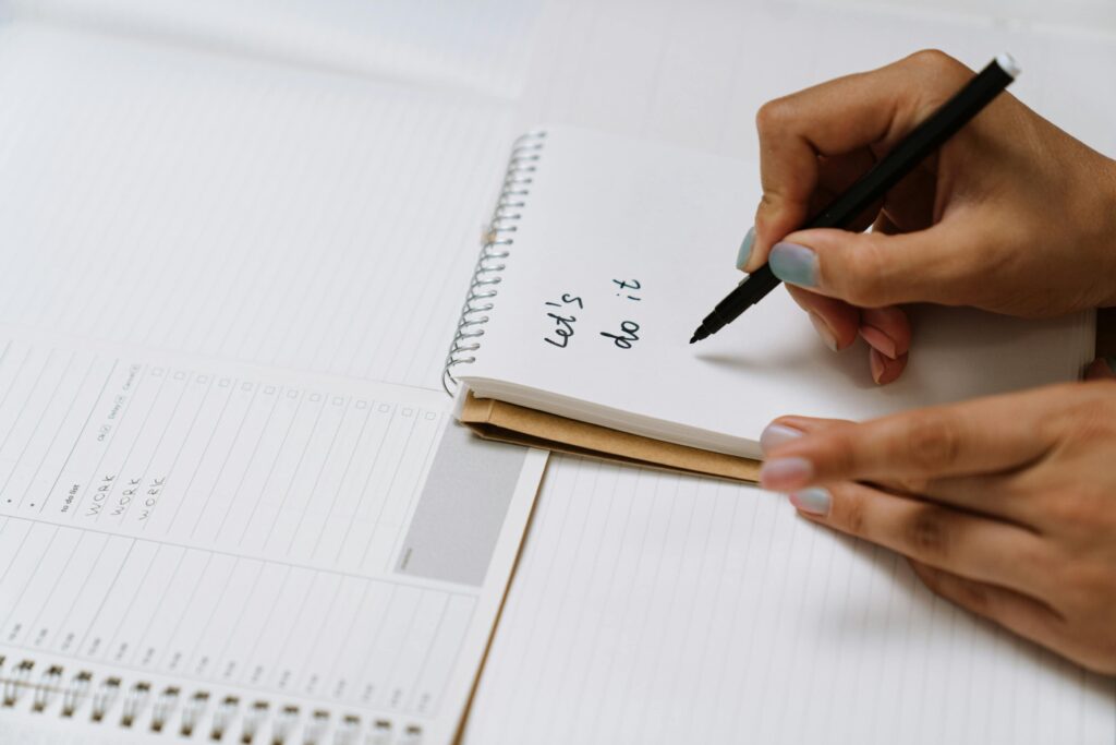 Close-up of hands writing 'Let's do it' on a notepad with a black pen, conveying motivation and planning.